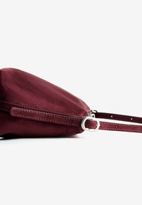 Burgundy suede crossbody bag with a flat shape, silver hardware, and a slim adjustable strap. Textured finish with stitching details.
