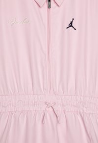 Vêtement rose à zip avec col, taille élastique, cordon de serrage et logo "Jordan" brodé près du haut. Texture de tissu lisse.