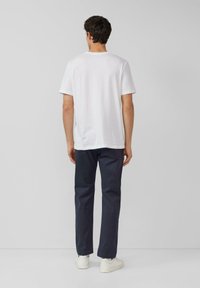 Weißes Baumwoll-T-Shirt mit kurzen Ärmeln, Rückansicht, kombiniert mit dunkelblauen Hosen und weißen Turnschuhen. Minimalistisches Design, keine Muster.