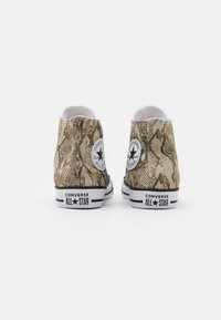 Tenisky Converse All Star ve vysokém provedení s béžovým a hnědým hadím vzorem, zobrazené zezadu na bílém pozadí.