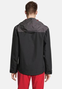 Schwarze wasserdichte Jacke mit grauem Oberteil, verstellbarer Kapuze und Bündchen. Glatte Textur und lässige Passform, kombiniert mit roten Hosen.