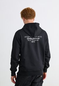 Sudadera con capucha negra con un logo en la parte trasera, que presenta un texto en blanco que dice "Dickies Workwear Co. Prendas de calidad diseñadas para resistir 1922."