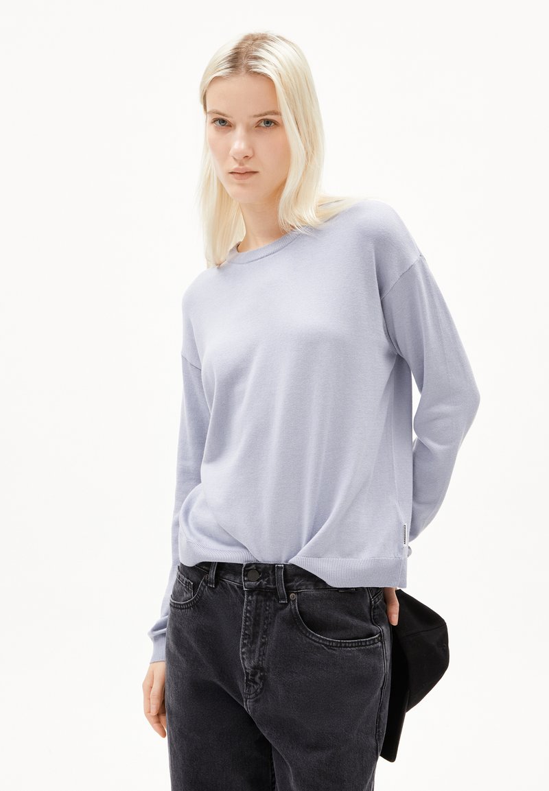 Helles blaues Strickpullover mit rundem Halsausschnitt und langen Ärmeln, kombiniert mit dunklen schwarzen Jeans. Der Pullover hat eine lockere Passform.