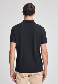 Svart pikétröja i bomull, med klassisk krage och korta ärmar. Enfärgad design utan synliga mönster eller detaljer.