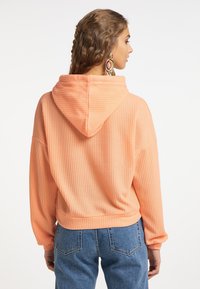 Pullover con cappuccio, texture in colore pesca chiaro, caratterizzato da una vestibilità ampia, orlo a costine e maniche lunghe. Indossato con jeans blu, mostra vista posteriore.