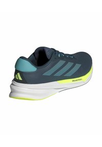 Herren Sneaker in dunkelblau mit hellblauen Akzenten und einer leuchtend gelben Sohle. Präsentiert ein Design mit drei Streifen und einer strukturierten Oberfläche mit Schnürsenkeln.