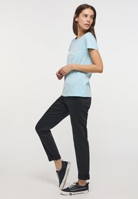 Világoskék, rövid ujjú póló grafikai mintával, sötét tengerészkék slim-fit nadrággal és sötétkék vászon sportcipővel párosítva.