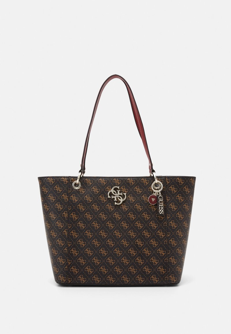 Sac fourre-tout marron et noir à motifs avec poignées marron, breloques argentées avec logo et étiquette décorative de la marque Guess sur fond blanc.