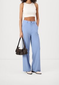 Pantalon large bleu clair à texture lisse, associé à un débardeur blanc court. Un petit sac à bandoulière marron foncé accentue la tenue.