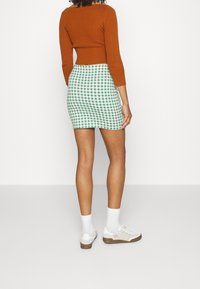 Gonna mini a quadretti verdi e bianchi, abbinata a un maglione lungo a coste marrone e sneakers bianche con tre strisce.