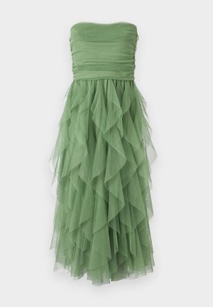 Rochie verde fără bretele, cu un corset plisat și o fustă cu volane stratificate, realizată dintr-un material ușor. Textura semi-transparentă accentuează fluiditatea.