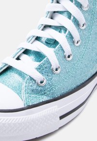 Κοντινό πλάνο αθλητικού  παπουτσιού με υφή από πράσινο γκλίτερ, άσπρα κορδόνια, μεταλλικά κορδόνια, λευκό λαστιχένιο προφυλακτήρα στα δάχτυλα και λευκή σόλα με μαύρες ρίγες.