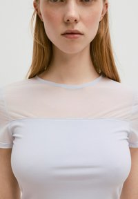 Lichtblauw aansluitend top met doorschijnende korte mouwen en een solide lichaam. Kenmerkt zich door een ronde halslijn en een gladde textuur overal.