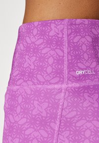 Fialové sportovní legíny s texturovaným květinovým vzorem, mají výrazný pas a bílé logo "DRYCELL".