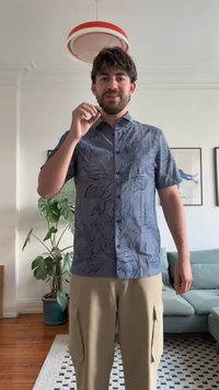 Camisa de manga curta em tecido azul com um padrão floral escuro, com fecho de botões à frente, usada com calças cargo em tom bege claro.