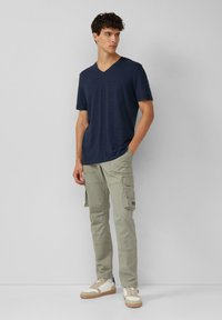 Granatowa koszulka typu V-neck, lekka tkanina, zestawiona z jasnoszarymi spodniami cargo z wieloma kieszeniami oraz białymi trampkami z brązowymi akcentami.