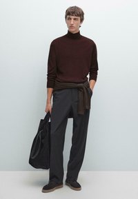 Burgundy polotröja, mörkgrå vida byxor och mörk axelväska. Bruna texturerade detaljer på skorna. Minimalistisk miljö.