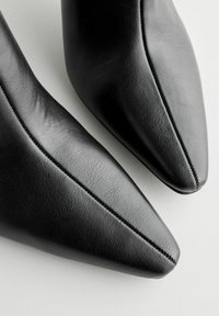 Scarpe nere in pelle con punta affusolata, caratterizzate da una texture liscia, cuciture decorative lungo la cucitura e un design elegante e moderno.