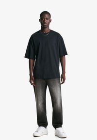 Schwarzes oversized T-Shirt mit kurzen Ärmeln, kombiniert mit jeans in verblichenem Schwarz und weißen Sneakern, akzentuiert durch eine schlichte Halskette.