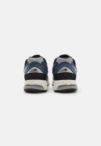 Sneakers blu navy con dettagli grigi, dotati di una tomaia in rete, collo imbottito e suola ammortizzata, mostrano la vista posteriore e il dettaglio del logo.