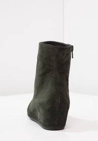 Bottine à talon compensé en daim vert foncé au toucher lisse, avec une fermeture éclair sur le côté et une forme profilée pour un look ajusté.