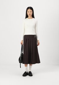 White ribbed knit sweater, brown pleated midi skirt with side buckles, black shoulder bag, white socks, and black shoes.