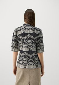 Blusa nera con intricati motivi geometrici argento. Maniche corte con bordi a scallop, tessuto leggero e vestibilità comoda.