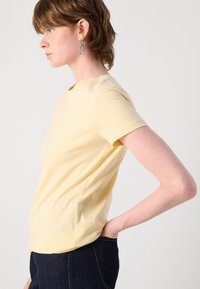 T-shirt giallo a maniche corte con colletto rotondo, realizzato in tessuto morbido, con un logo discreto sul fronte e una forma aderente.