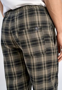 Geruite broek in donker groen en beige, met een elastische tailleband, zijzakken en een logo-patch op de achterzak.
