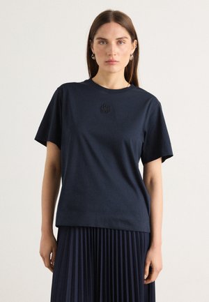 Marineblaue Baumwoll-T-Shirt mit kurzen Ärmeln, ausgestattet mit einem kleinen gestickten Logo auf der Brust. Glatte Textur und entspannter Schnitt.