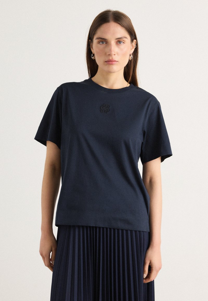 Navy blue cotton t-shirt with short sleeves, featuring a small embroidered logo on the chest. Smooth texture and relaxed fit.