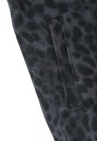 Primo piano di un tessuto in denim nero con un'apertura per tasca verticale cucita nel materiale.