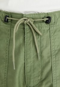 Light green shorts with an elastic waistband, featuring a braided drawstring and two side pockets. Smooth cotton fabric with subtle texture.