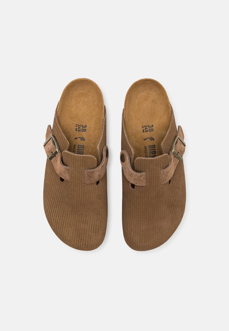 Braune Wildlederschuhe mit strukturiertem Obermaterial, seitlichem Schnallenverschluss und Ausschnitten zur Belüftung. Das Innere verfügt über ein Korkfußbett.