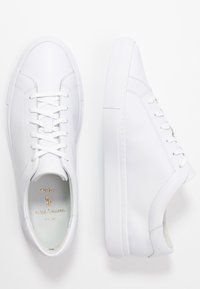 Vita lädersneakers med slät yta, rund tå, flat gummisula och snörningsdesign. Guldlogotyp på insidan av skon.