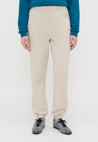 Beige sweatpants met elastische tailleband en boorden. Gemaakt van zacht materiaal, met een gladde textuur en een ontspannen pasvorm. Gekozen in combinatie met grijze sneakers.