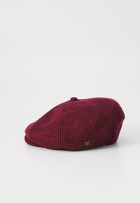 Burgundy wool beret with a rounded shape, featuring fine stitching details and a small metal emblem on the side. Soft texture.