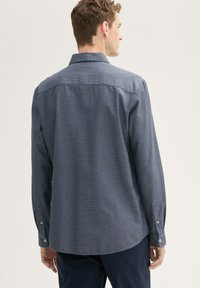 Camisa de manga larga con botones, de color azul oscuro con un sutil patrón texturizado. Presenta un cuello extendido, dobladillo redondeado y puños abotonados.