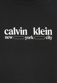 Calvin Klein logotipas su stilizuotu „new york city“ tekstu ant juodos medžiagos, baltomis raidėmis ir dviem tuščiomis stačiakampių kontūromis.