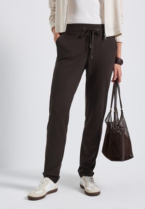 Brown jogger pants with a drawstring waist, side pockets, tapered leg, paired with white sneakers and a dark mesh handbag.