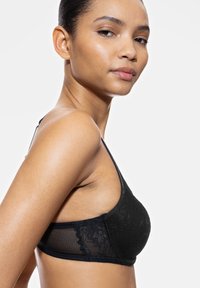 Bralette de encaje negro con tejido texturizado, paneles de malla semitransparente, tirantes ajustables y un detalle de borde festoneado.