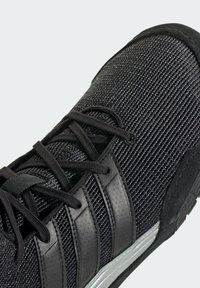 Black athletic shoe with textured mesh upper, black laces, and three matte black stripes. Features a contrasting silver accent near the sole.
