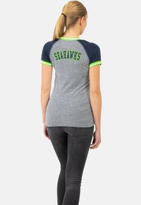 T-shirt gris clair avec des manches raglan bleu marine et des accents verts. "SEAHAWKS" imprimé en lettres majuscules au dos.