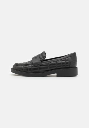 Mocassin en cuir noir avec motif matelassé et petit talon carré, vu de profil sur fond blanc uni.