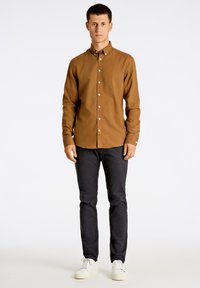 Bruine overhemden met een slim fit, lange mouwen, witte knopen, gecombineerd met marineblauwe broek en witte sneakers op een effen achtergrond.