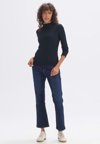 Schwarzes gestreiftes Langarmtop mit hohem Kragen, kombiniert mit dunkelblauen weiten Jeans und weißen Sneakers. Einfaches, klares Design.