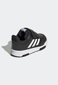 Černá sportovní bota s texturovaným svrškem, bílými akcenty a suchým zipem. Vyznačuje se zaobleným tvarem a gumovou podrážkou pro lepší grip.