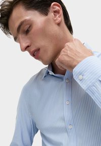 Lichtblauw gestreepte overhemd gemaakt van zachte stof met een spitse kraag en knoopmanchetten. Gevoerd met verticale witte strepen en knoopdetails.