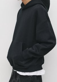 Černá pulovrová mikina s kapucí vyrobená z bavlny, s přední kapsou, žebrovanými manžetami a lemem. Měkká textura s pohodlným střihem.