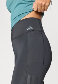 Høj talje, sorte atletiske leggings med tekstureret stof, tonale syninger og et diskret mærkelogo nær taljebåndet.